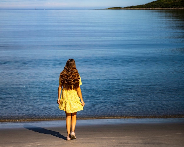 Photo beautiful girl in a yellow dress stares at the sea on a beach surrounded by mighty mountains, senja