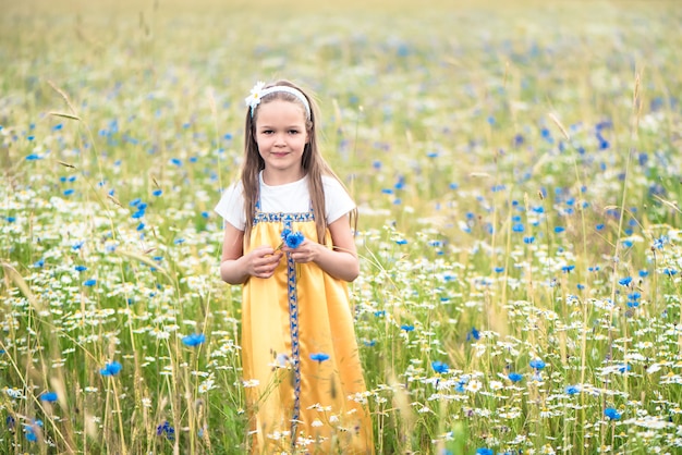 黄色のサラファンで美しい少女は、野生の花の草原を歩く