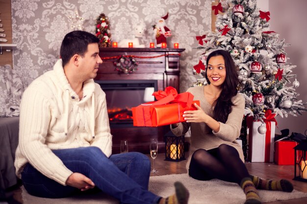 クリスマスの日に彼女のボーイフレンドにギフトボックスを与える美しいガールフレンド。愛を込めてクリスマスを祝います。