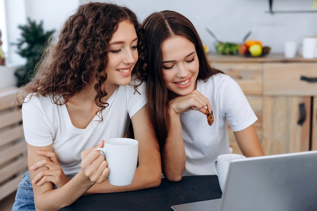 Beautiful girls leaning on each other drinking tea with cookies