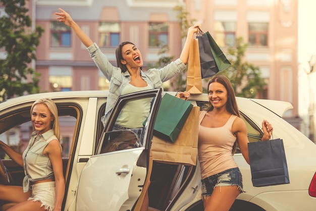 Photo beautiful girls peeking out of a car with bags