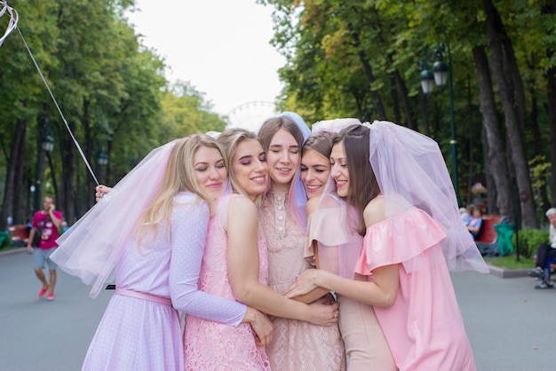 beautiful girls in pink dresses celebrating bachelorette party in the park and hugging