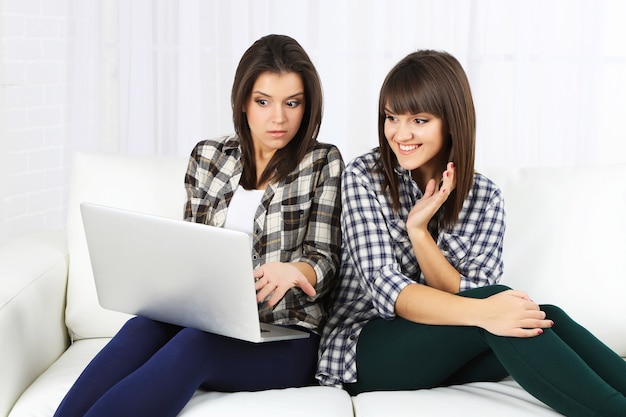 Beautiful girls twins sitting on sofa with notebook