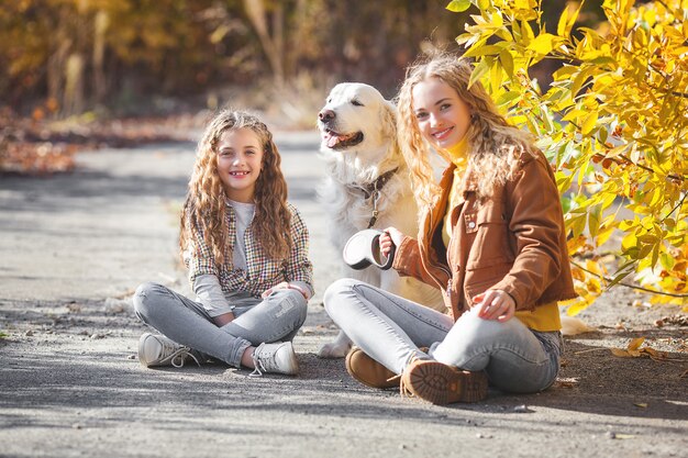 Beautiful girls with golden retriever. Two sisters outdoors having fun.pet owners in autumn.