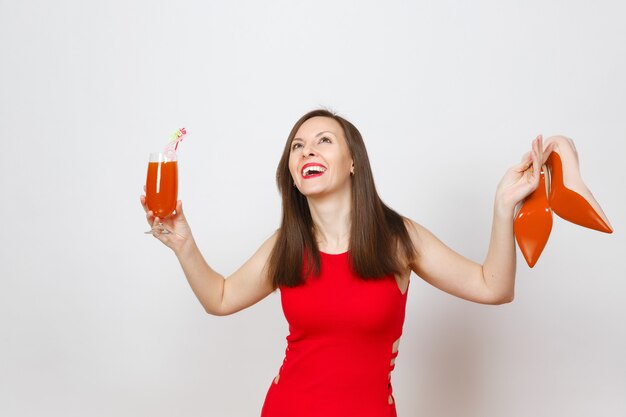 Beautiful glamour fashionable young brown-hair woman in red dress holding glass of drink cocktail, beige shoes with red sole of her shopping isolated on white background. Copy space for advertisement.