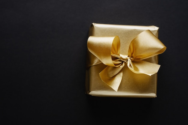 Photo beautiful golden box christmas gift with golden ribbon on dark.