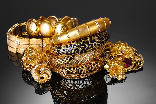 Красивые золотые браслеты, кольца и украшения на сером фоне