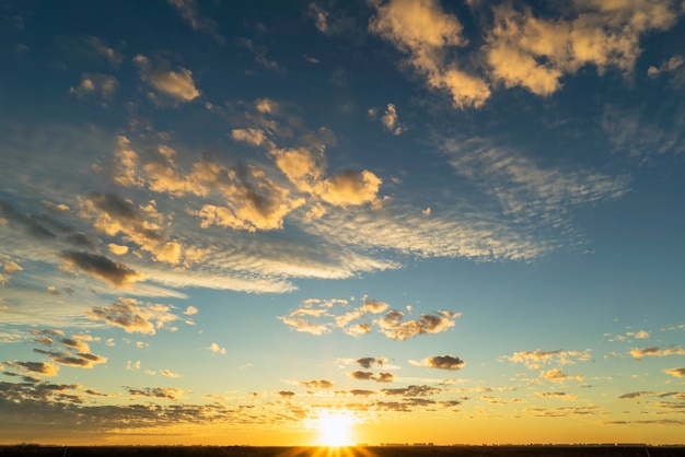 Beautiful Golden clouds illuminated by the rays of the sun at sunset float across the yellow-blue sky.