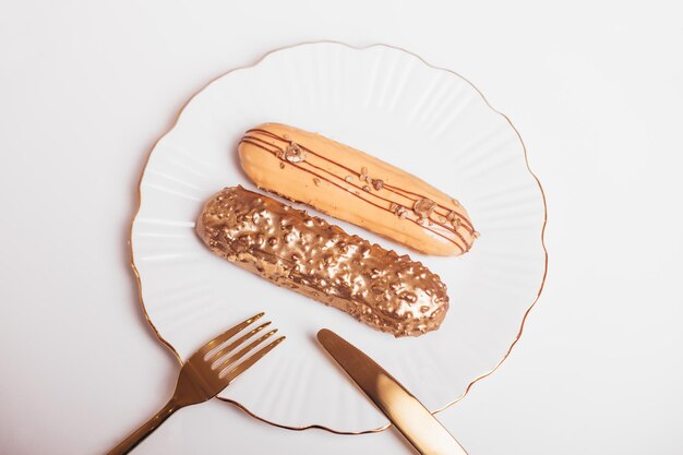 Beautiful golden colored eclairs on plate with knife and fork on white background