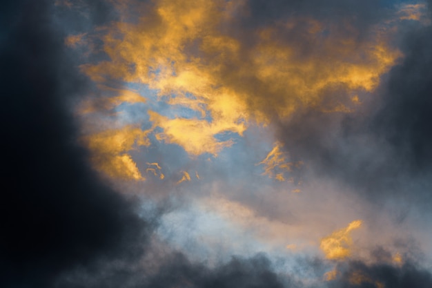 Bellissime nuvole temporalesche dorate illuminate da raggi che scompaiono al tramonto e nuvole scure flo...