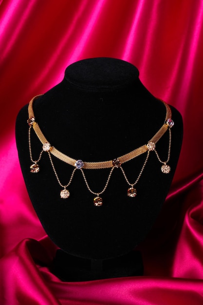 Beautiful golden necklace on mannequin on red silk fabric