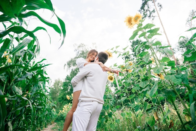 Beautiful gorgeous woman and stylish handsome male, rustic couple in a sunflower field kissing, tender