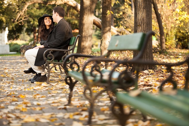 Beautiful gourgeous couple sitting on a bench in autumn park