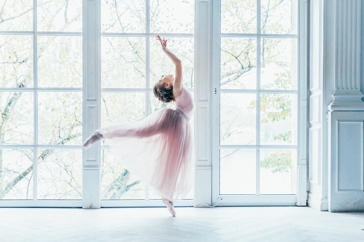 Photo 白い光のホールの大きな窓の近くのピンクのチュチュスカートで美しい優雅なバレリーナ練習バレエの位置