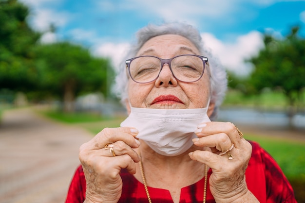 Beautiful gray-haired old grandmother in a medical mask with glasses and straightens the mask and looks. End pandemic. Covid-19. Coronavirus.