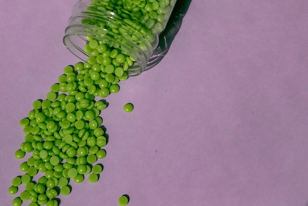 Beautiful green wax granules with aloe extract for depilation are poured onto a light purple background from a transparent jar epilation depilation removal of unwanted hair place for text