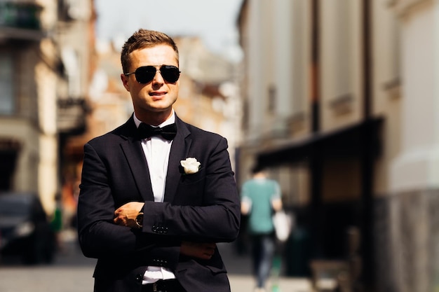 Beautiful groom in a black suit and sunglasses on the background
