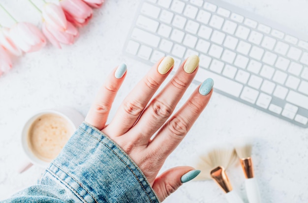 Foto belle mani femminili curate con unghie blu pastello e gialle concetto di salone di bellezza per manicure posto vuoto per il testo vista dall'alto