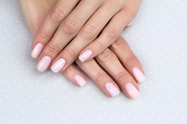 Beautiful groomed woman's hands with feminine nails on the light gray table.