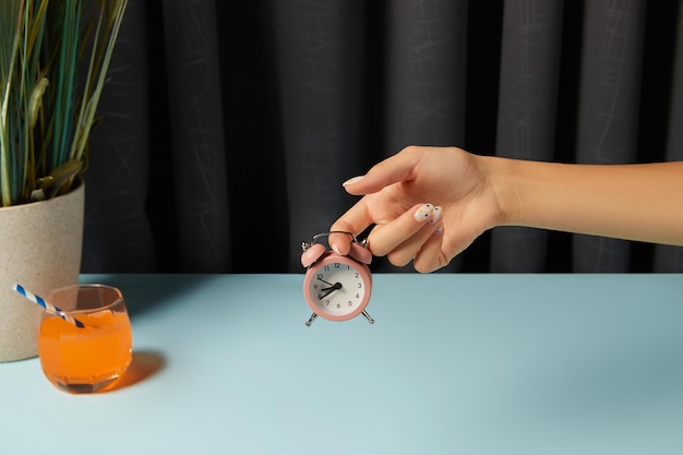 Beautiful groomed womans hand holding alarm clock over blue table