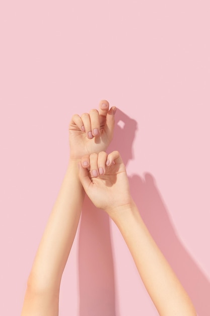 Beautiful groomed womans hands with pink matte nail design on a pink background manicure pedicure