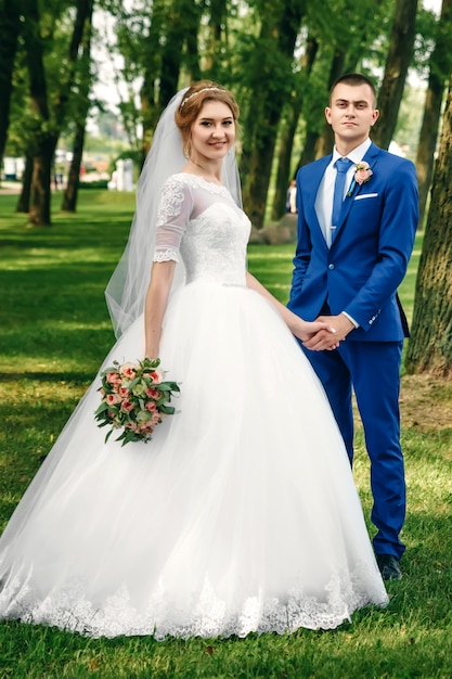 Красивый парень и девушка, невеста в белом свадебном платье, жених в классическом синем костюме на фоне природы. Свадьба, создание семьи.