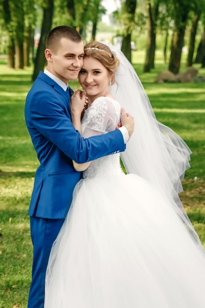 美しい男と女、白いウェディングドレスの花嫁、自然を背景に古典的な青いスーツの新郎。結婚式、家族の創造。