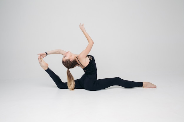 Beautiful gymnasts in black suits posing over white wall.