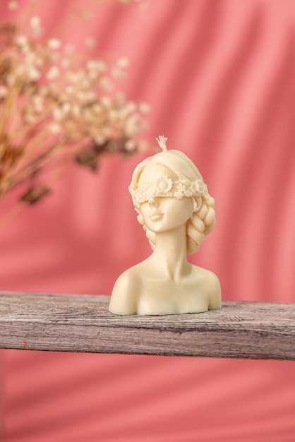 Beautiful handmade candle in the shape of a female body on a wooden stand and pink background