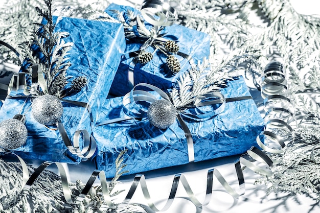 Beautiful handmade New Year presents in silver blue color. Christmas card with silver and blue background. Christmas decoration with pine, a fir tree and gift boxes. Close up.