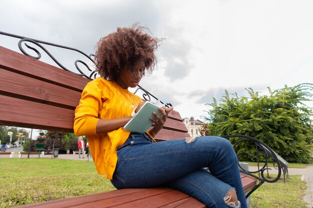 The Beautiful and happy African American woman in the park, makes notes in a notebook