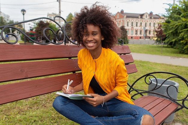 The Beautiful and happy African American woman in the park, makes notes in a notebook