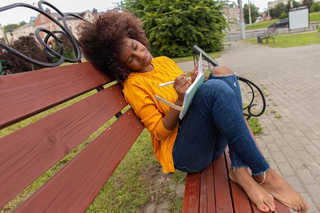 公園で美しく幸せなアフリカ系アメリカ人の女性は、ノートにメモを書きます