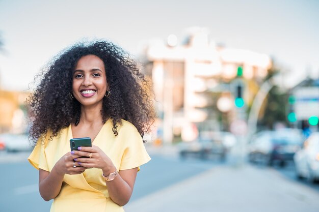 Beautiful happy Black Afro woman with positive and cheerful expression is looking to camera with holding a mobile phone includes copy space