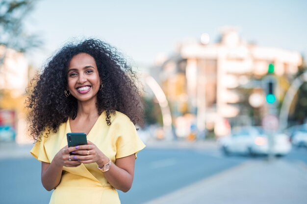 Beautiful happy Black Afro woman with positive and cheerful expression is looking to camera with holding a mobile phone includes copy space