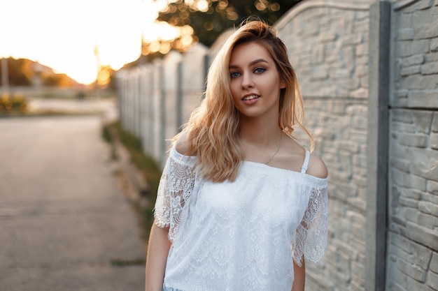 Красивая счастливая блондинка с улыбкой в винтажной белой футболке на закате