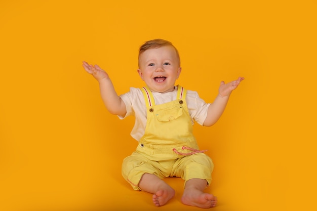 黄色いスーツを着た美しい幸せな青い目の小さな男の子は彼の側に彼の腕を広げた