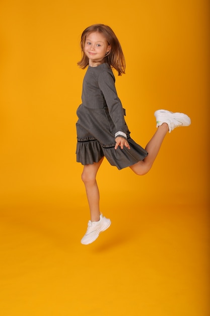 beautiful happy brownhaired girl in a gray school dress jumps yellow background