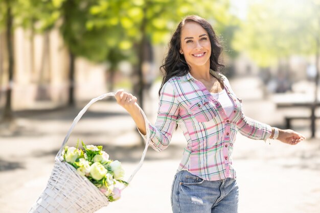 A beautiful happy brunette dances with joy in the streets of the city with a basket full of flowers