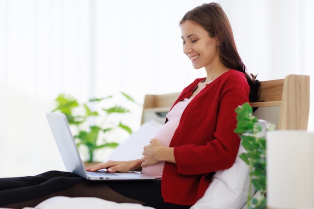 Foto una bella madre caucasica felice si siede a letto usando il suo computer portatile per cercare informazioni