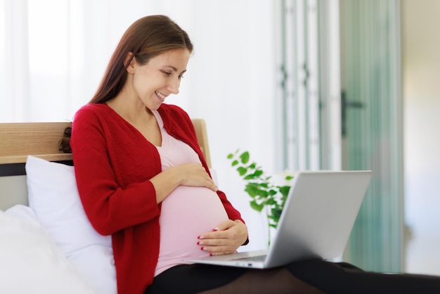 Una bella madre caucasica felice si siede a letto usando il suo computer portatile per cercare informazioni