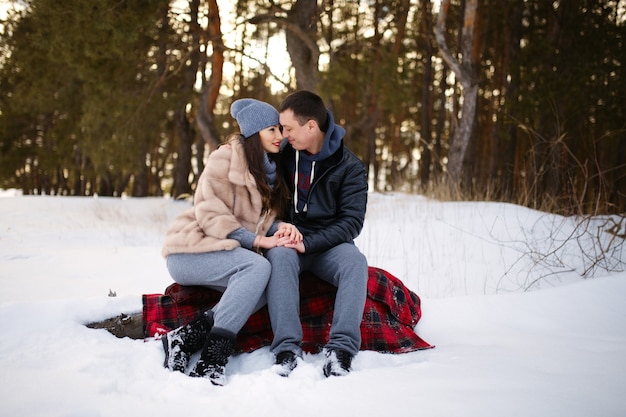 Beautiful and happy couple in love sitting on a blanket in winter in a snowy forest