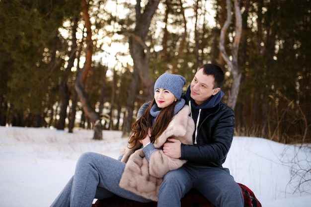 Beautiful and happy couple in love sitting on a blanket in winter in a snowy forest