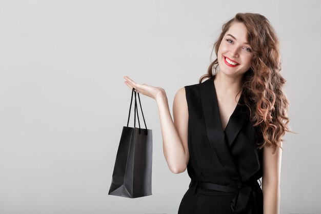 Beautiful happy curly woman in black elegant overall with shopping bag copy space