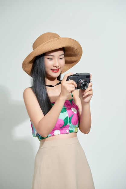 Photo beautiful happy cute asian woman in casual summer clothes takes photos holding retro photographic camera isolated on a white in hat