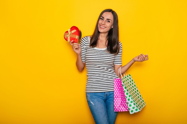 Beautiful happy excited brunette woman in casual clothes is posing with shopping bags isolated on yellow background