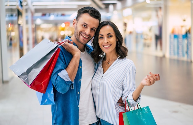 Bella coppia felice eccitata innamorata o famiglia con sacchetti di carta nelle mani mentre si cammina durante lo shopping nel centro commerciale