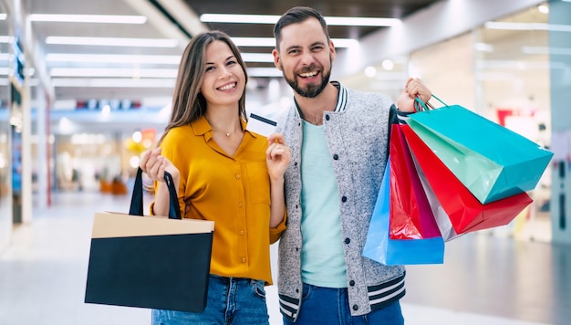 Beautiful happy excited couple in love or family with paper bags in hands while walking during shopping in the mall