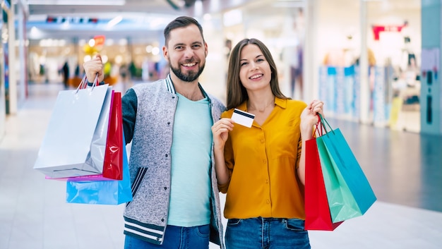 Beautiful happy excited couple in love or family with paper bags in hands while walking during shopping in the mall