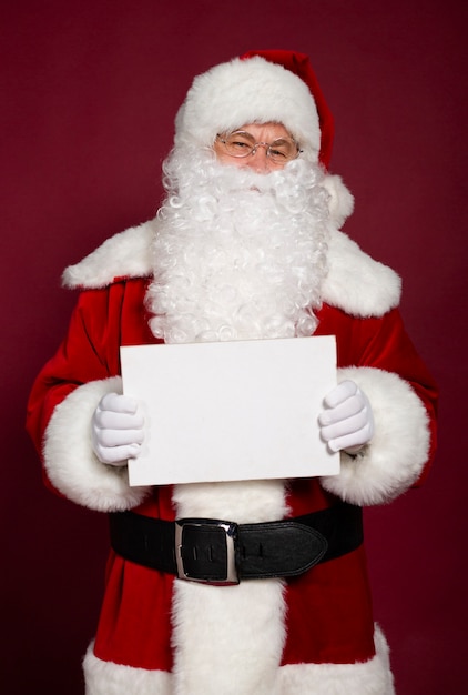 Il bello babbo natale emozionante felice sta proponendo e mostrando il bordo in bianco bianco nelle mani